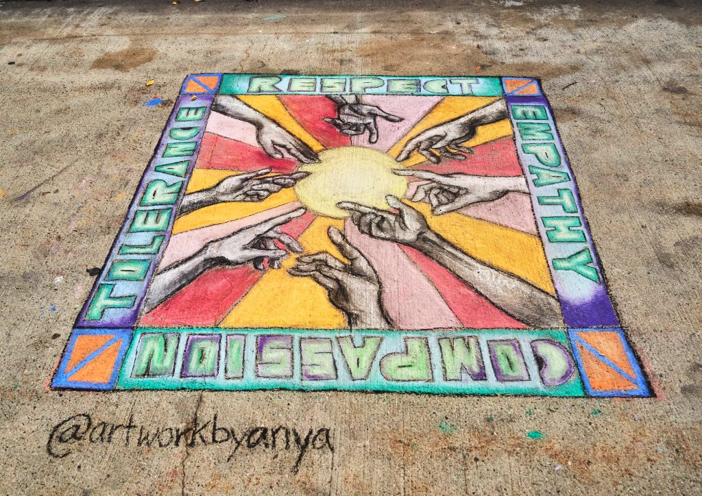 Photo of a chalk mural on a sidewalk. Mural depicts hands reaching into sun.
