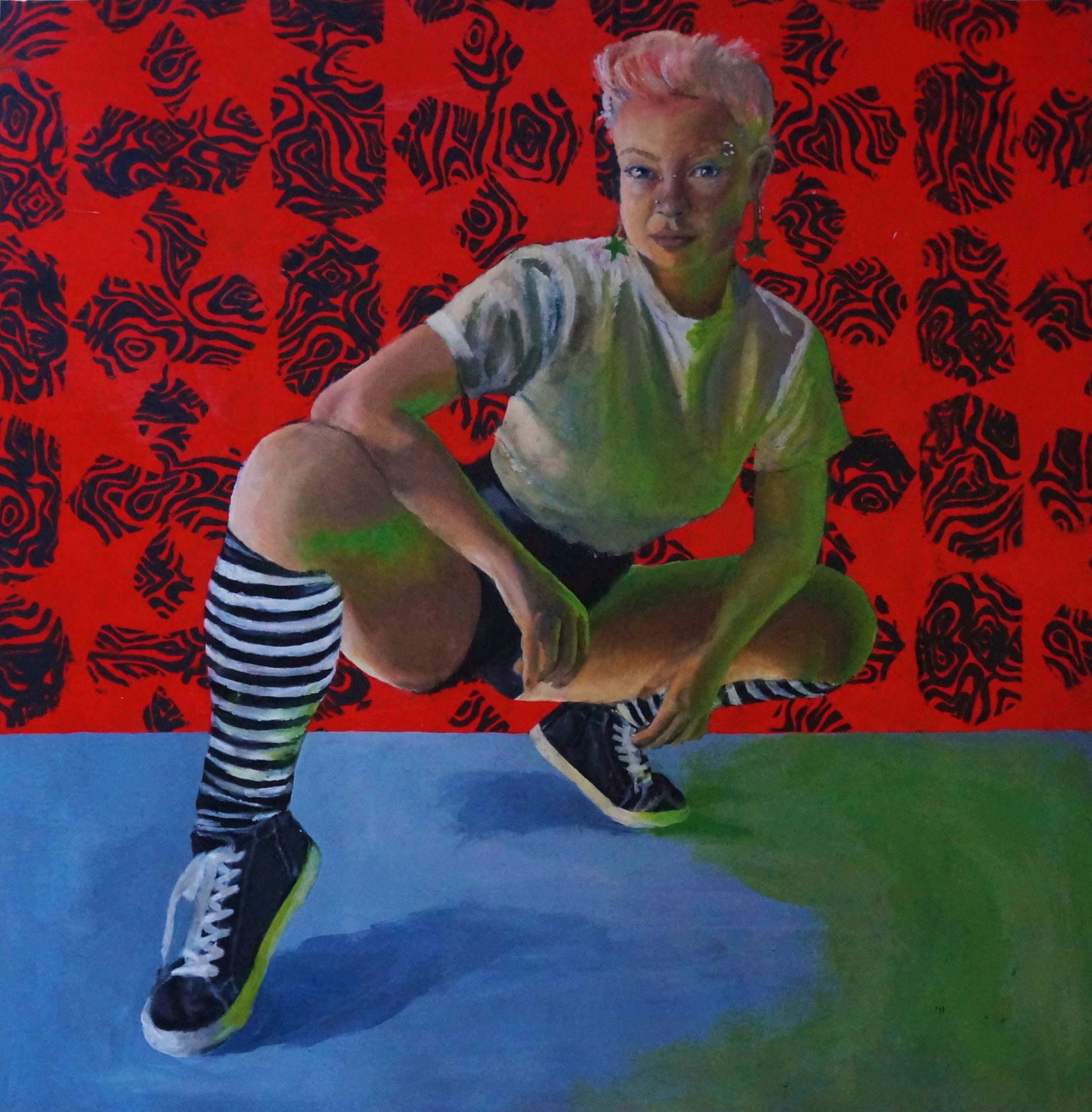 A woman with pink hair and striped socks crouches in front of a red background.